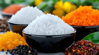 Fresh aromatic spices and seasonings in black ceramic bowls, colorful assortment including sea salt, saffron, black peppercorns and dried chili flakes on dark surface.