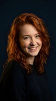 Happy young Caucasian woman with curly red hair smiling warmly in dark sweater against navy background for lifestyle and portrait photography.