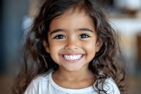 Young girl with curly dark hair and bright genuine smile wearing white shirt, closeup portrait showing joyful expression and natural beauty in soft lighting.