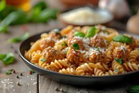 Homemade fusilli pasta with juicy meatballs in rich tomato sauce, garnished with fresh basil and grated parmesan cheese, served in dark plate on rustic wooden table.