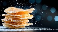 Crispy potato chips stacked with falling salt particles against dark background with bokeh lights, dramatic food photography for snack advertising.
