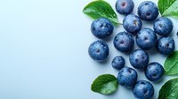 Fresh ripe blueberries with water drops and green leaves scattered on light blue background, macro view of organic berries with copy space.