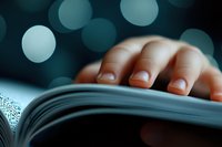 Fingers gently turning pages of open book against dark background with soft bokeh lights creating atmospheric reading mood for literature and education concepts.