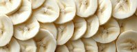 Fresh sliced banana pieces arranged in overlapping pattern, showing detailed texture and natural color of ripe fruit.
