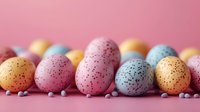 Colorful speckled Easter eggs in pastel pink, blue, and orange arranged in row on pink background with small decorative candies, festive spring holiday concept.