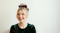 Young woman with platinum blonde hair and fair complexion wearing dark green velvet top and tortoiseshell sunglasses on head, smiling against neutral background for portrait use.