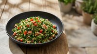 Tabbouleh salad with fresh parsley, tomatoes, and bulgur wheat in black bowl on wooden surface for culinary and food styling projects.