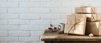 Kraft paper wrapped gift boxes tied with twine stacked on rustic wooden shelf against white brick wall with copy space for holiday shopping and seasonal promotions.