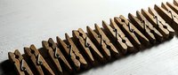 Row of wooden clothespins arranged in line on white surface for laundry organization and household storage solutions.