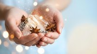 Hands holding aromatic spices cinnamon sticks and star anise with warm bokeh lights creating cozy atmosphere for cooking baking and holiday recipes.