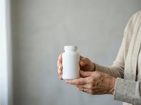 Senior woman with brown skin holding blank white supplement bottle against neutral gray background for healthcare and wellness product packaging mockup.