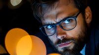 Professional bearded businessman with glasses working late at night with warm bokeh lights creating atmospheric office environment for corporate projects.