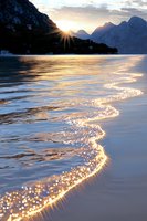 Sunlight sparkles on gentle waves at mountain lake during golden sunset, creating shimmering reflections across water surface against dramatic alpine peaks.