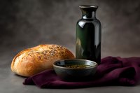 Fresh artisanal bread with poppy seeds served with olive oil and balsamic vinegar in dark ceramic bowl on burgundy linen napkin against moody background.