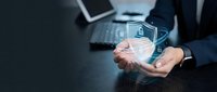 Businessman holding holographic digital security shield icon above palm in modern office workspace representing cybersecurity and data protection technology.