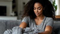 Young African American woman relaxing on couch at home petting fluffy gray cat in cozy living room interior. Casual lifestyle moment with pet companion.