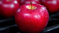 Fresh red apple with water drops on glossy surface, macro photography showing detailed texture and natural moisture against dark background.