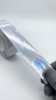 Reflective safety tape with holographic hexagonal pattern unrolled on white surface, showing iridescent blue and silver colors. Used for visibility, safety marking, and industrial applications.