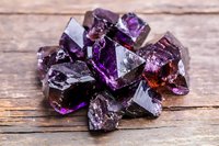 Raw purple amethyst crystal cluster with natural faceted gemstone formations on rustic wooden background for healing and meditation practices.