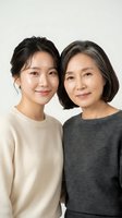 Two generations of Asian women embracing warmly, mother and adult daughter sharing intimate family moment against neutral background for lifestyle content.