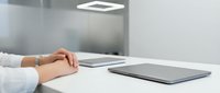 Professional businesswoman hands folded on modern white desk with laptop in minimalist office workspace for corporate presentations and meetings.