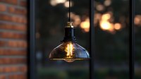 Vintage industrial pendant lamp with glowing edison bulb against blurred sunset and brick wall background creates cozy atmospheric lighting.