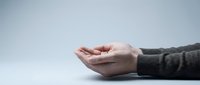 Cupped hands of a Caucasian person in a gray sweater reaching out on a light background, symbolizing giving, receiving, or asking for help.