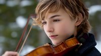 Young musician playing violin outdoors in winter setting with soft natural bokeh background, showing artistic expression and musical talent during performance.