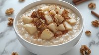 Creamy oatmeal topped with diced pears, walnuts and cinnamon in white ceramic bowl on marble surface, healthy breakfast porridge with fresh fruit.