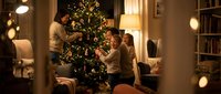 Family decorating Christmas tree together in warm living room with festive lights and cozy home interior ambiance.