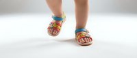 Child wearing colorful rainbow striped sandals walking on white background. Summer footwear for kids with bright multicolored straps and comfortable sole design.