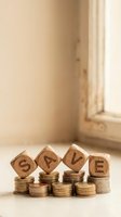 Wooden blocks spelling SAVE placed on stacks of coins representing financial savings and money management concepts for budgeting and investment planning.
