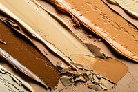 Smeared foundation makeup swatches showing different skin tone shades in brown and beige colors with creamy texture close up macro photography.