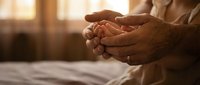 Senior woman hands cupped together in prayer or meditation pose with warm sunlight streaming through window creating peaceful spiritual moment.