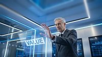 Senior Caucasian businessman in dark suit touching holographic VALUE interface in futuristic blue-lit office environment with digital technology displays.