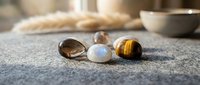 Three polished gemstones smoky quartz moonstone tiger eye on textured surface with blurred kitchen background warm natural lighting meditation wellness.