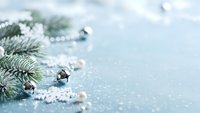 Silver Christmas bells and white pearls scattered with evergreen fir branch on sparkling blue background for holiday greeting cards and winter decorations.