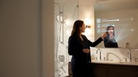 Young woman applying makeup in modern bathroom mirror with elegant lighting and marble countertop for morning beauty routine and self-care rituals.