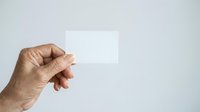 Hand holding blank white card or paper against neutral background, suitable for mockups, presentations, advertising campaigns, and business branding materials.