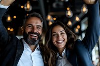 Happy mature businessman and young businesswoman celebrating success with raised arms in modern office with warm lighting atmosphere.