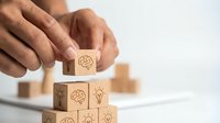 Hands stacking wooden blocks with brain and light bulb icons, symbolizing creativity, innovation, and strategic thinking in business.