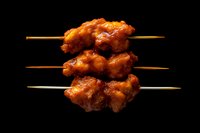 Glazed chicken yakitori skewers with sweet and savory sauce on wooden sticks against black background, isolated Asian cuisine food photography.