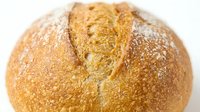 Freshly baked round artisan bread loaf with crispy golden crust and flour dusting, isolated on white background for bakery, food, and culinary design projects.