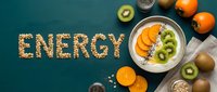 Granola spelled word ENERGY beside a bowl of yogurt topped with kiwi and persimmon slices on a teal background, healthy breakfast concept.