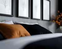 Modern bedroom interior with black and orange accent pillows on bed, minimalist framed artwork on gray wall, soft natural lighting creates cozy atmosphere.