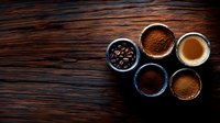 Fresh roasted coffee beans and ground coffee varieties in ceramic bowls with hot espresso on rustic wooden background, top view with copy space.