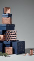 Stack of geometric gift boxes in copper and navy blue with metallic accents and ribbon, modern packaging design for holidays and special occasions.
