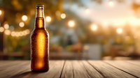 Cold beer bottle with condensation on wooden table against blurred warm bokeh lights background for restaurant or bar menu design.