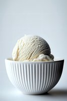 Creamy vanilla ice cream scoop served in elegant white ribbed ceramic bowl against light background, minimalist food photography composition for dessert menus.
