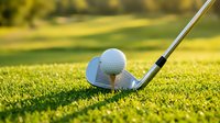 Golf club and ball on green grass course with warm sunlight creating golden hour atmosphere for sports and recreation activities.